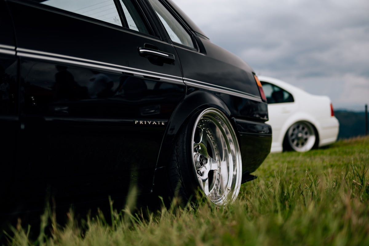 Low-riding cars are parked in a grassy field.